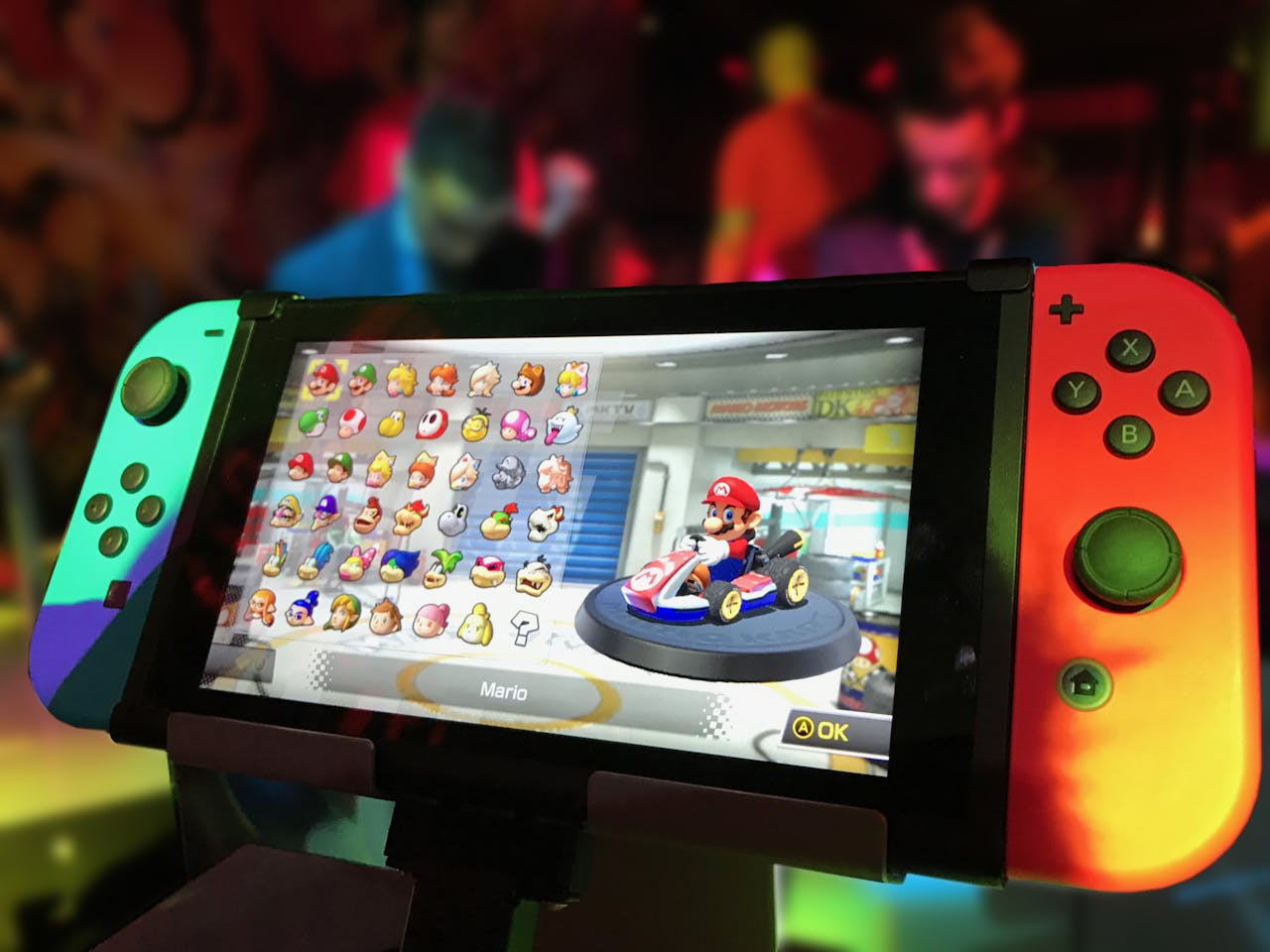 classes-02 Close-up of a Nintendo Switch showing Mario Kart selection screen, gaming atmosphere in the background.